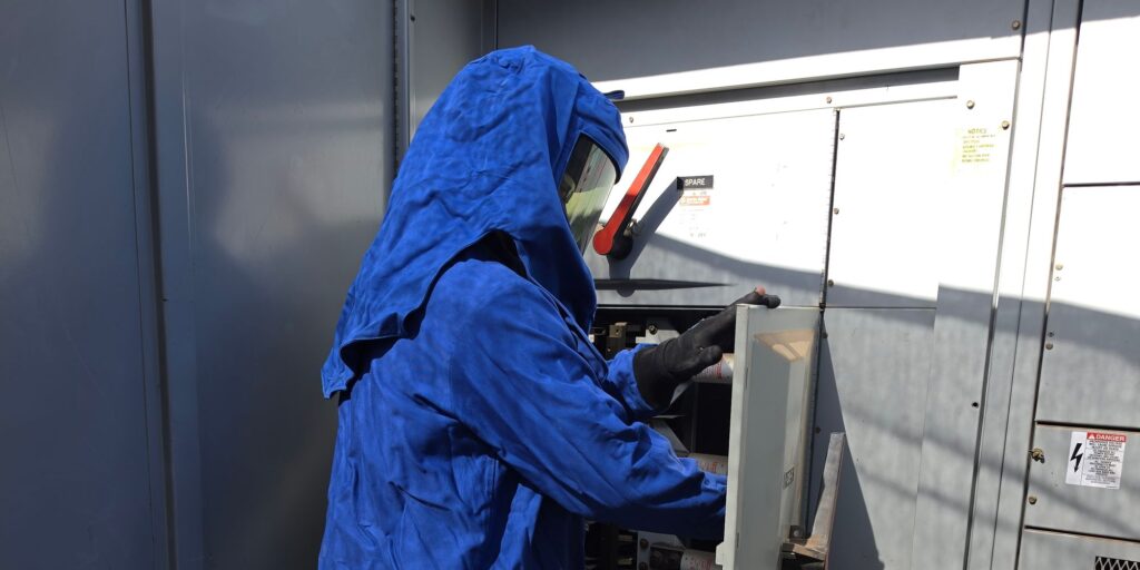 Technician in arc flash PPE performing a commercial service upgrade at switchgear